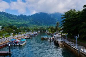 Malaysia storstad och paradisstrand Tioman-3 | Kenzan Travel Boats docked at a canal marina with green hills and cloudy blue sky beyond the waterway.